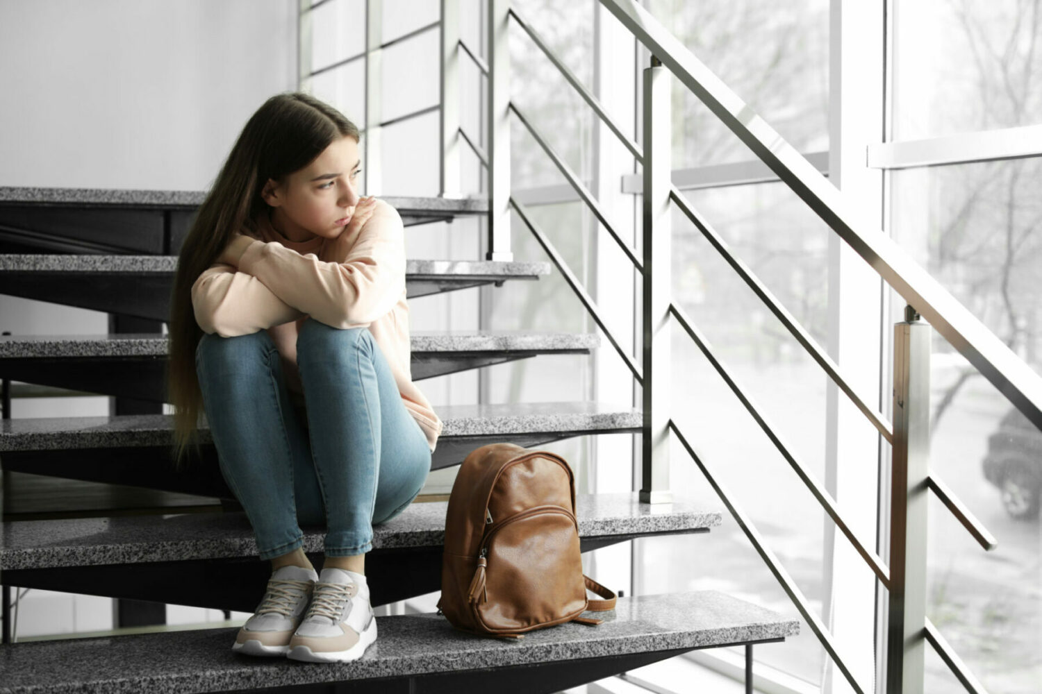 teenage girl looking unhappy with her backpack sitting on the stairs
